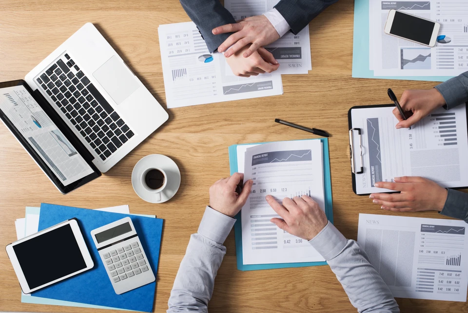 Réunion de travail en intérieur avec trois personnes analysant des rapports financiers sur table en bois