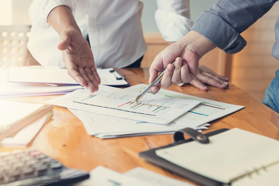 Réunion de travail en intérieur où deux professionnels analysent des documents financiers sur table en bois