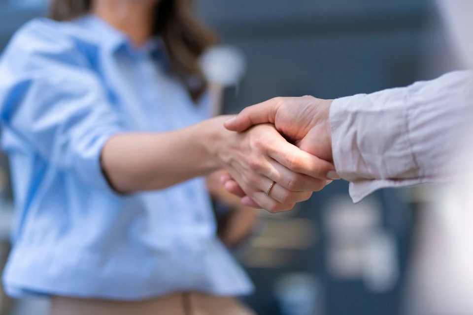 Poignée de main professionnelle entre deux personnes en environnement d'affaires, l'une portant une chemise bleue claire, l'autre une chemise blanche