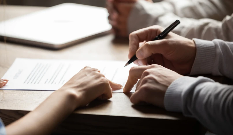 Photographie d'un expert-comptable dans son bureau, assis à son bureau face à un client, en train d'examiner ensemble des documents financiers ou un bilan comptable. La scène doit montrer une interaction professionnelle authentique, sereine et attentive, reflétant la relation de confiance et la proximité. L'atmosphère doit être celle d'un vrai cabinet comptable avec documents, dossiers et outils professionnels visibles, sans artifices ni mise en scène.