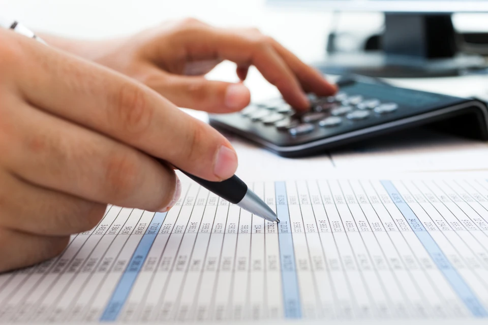 Personne travaillant sur documents comptables et fiscaux, utilisant calculatrice et stylo pour remplir formulaires administratifs sur bureau